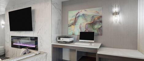 A modern hotel room with a marble wall, a flat-screen TV, a desktop computer, and a large abstract painting.