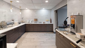 A modern kitchen with marble countertops, wooden cabinets, and a waffle maker. - La Quinta Inn & Suites by Wyndham Tucumcari (Tucumcari)