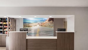 A reception desk with a scenic mural, a wooden counter, and a shelf with snacks. - La Quinta Inn & Suites by Wyndham Tucumcari (Tucumcari)