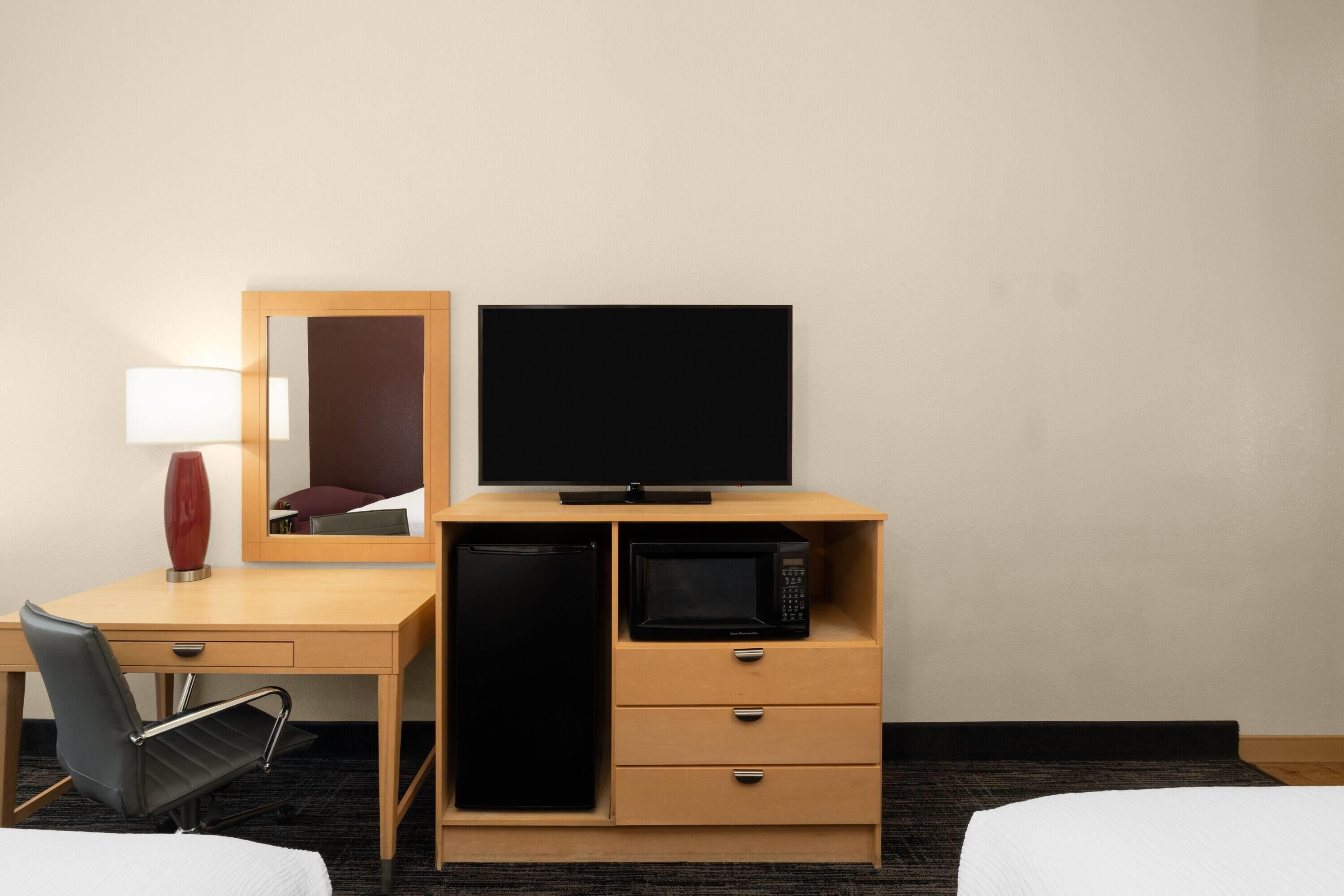 A hotel room with a bed, a desk with a chair, a television, a microwave, and a mirror.