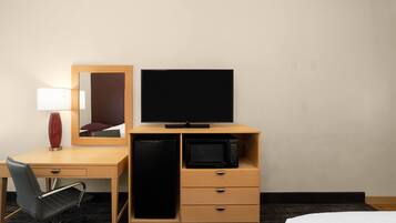 A hotel room with a bed, a desk with a chair, a television, a microwave, and a mirror.