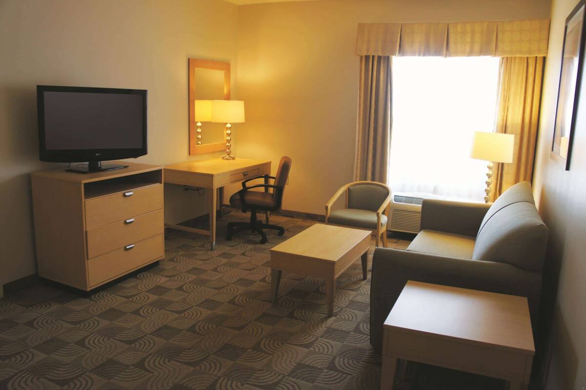 Habitación de hotel con televisión, escritorio, silla, sofá y ventana con cortinas.