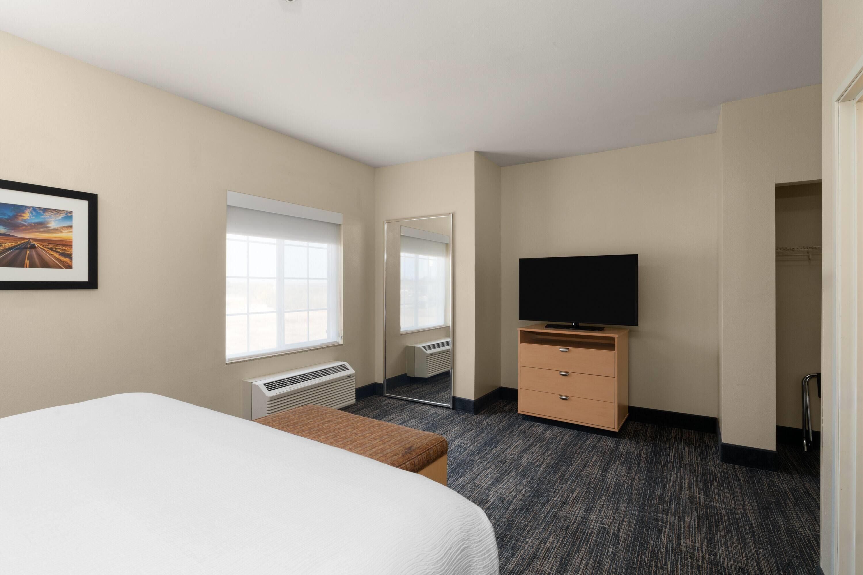 Una habitación de hotel con cama, televisión, cómoda, espejo y ventana.