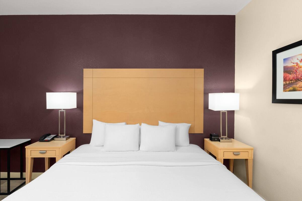 Habitación de hotel con una cama grande, dos mesitas de noche con lámparas, un teléfono y un cuadro en la pared.