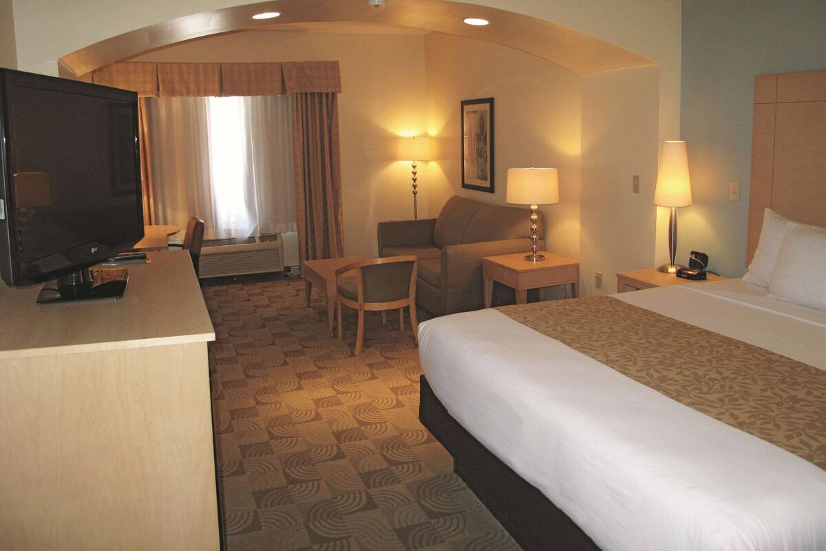 Habitación de hotel con cama, escritorio, televisión, silla y dos lámparas.