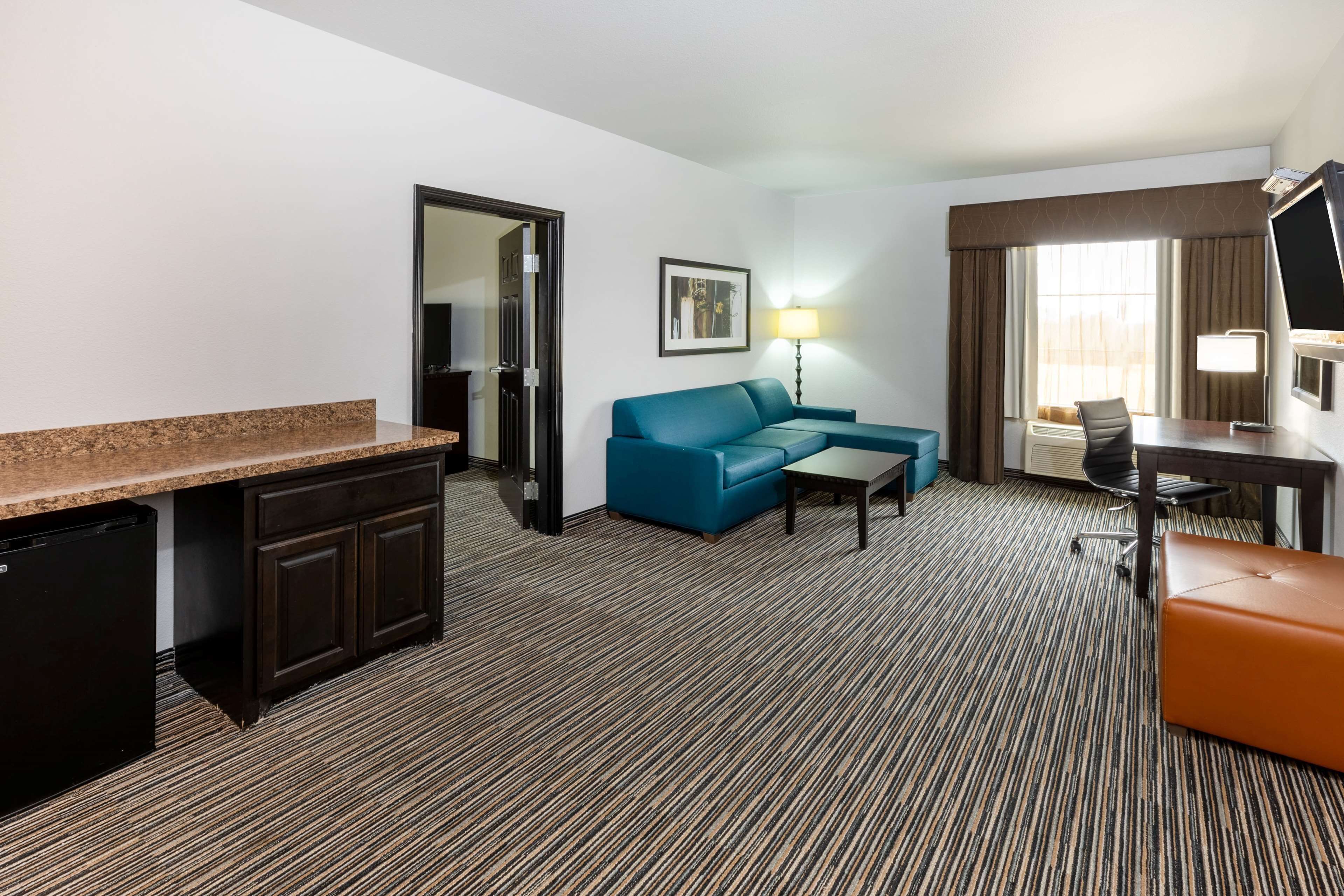 A hotel room with a kitchenette, a blue sofa, a desk with a chair, and a television.