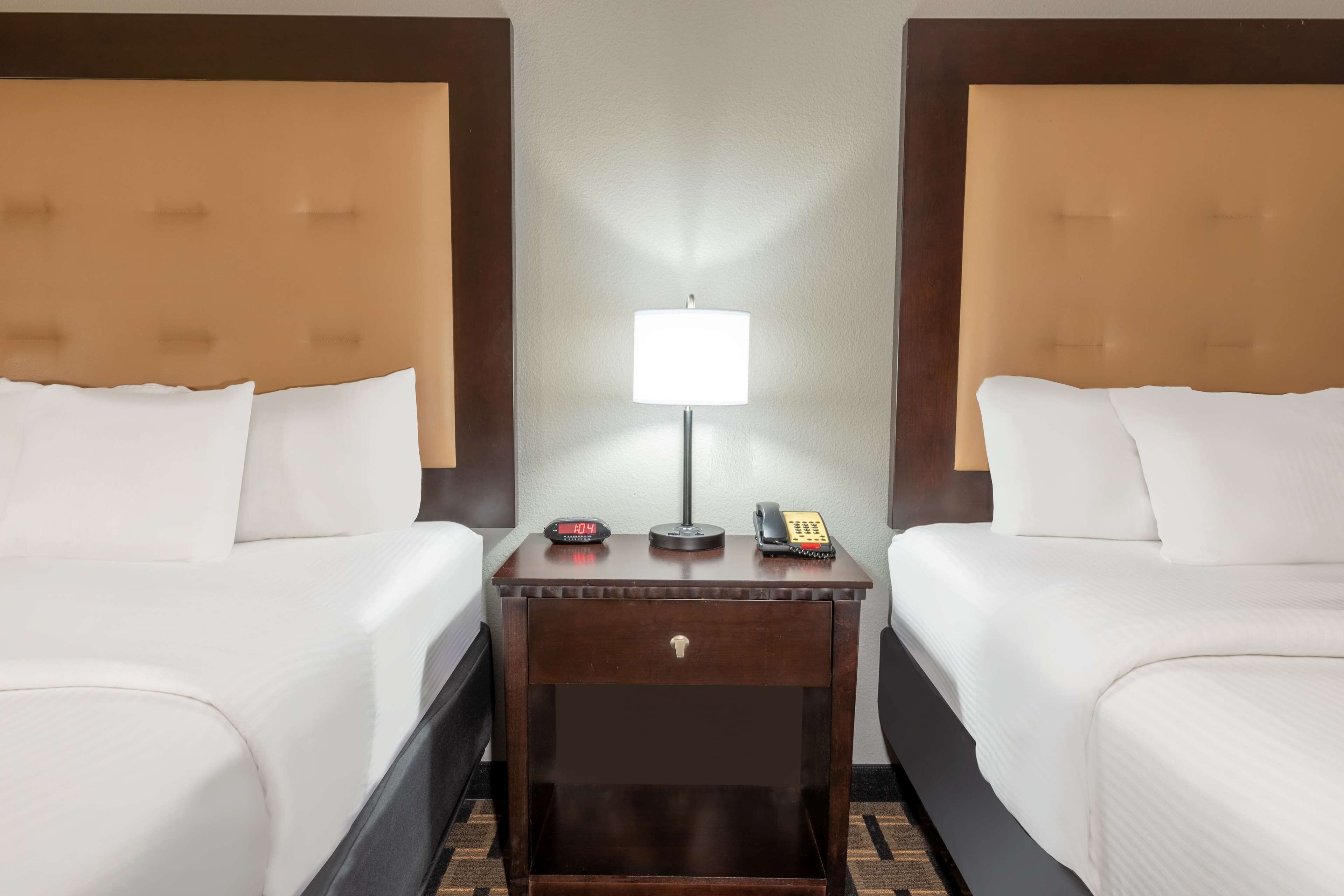 A hotel room with two beds, a nightstand with a lamp, a clock, and a telephone.