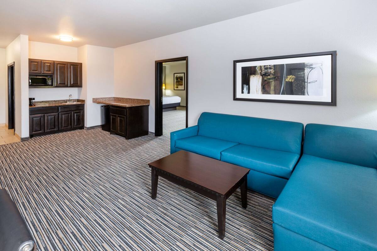 Ein modernes Wohnzimmer mit einem blauen Sofa, einem Couchtisch und einem durch einen offenen Durchgang einsehbarer Küchenbereich.
