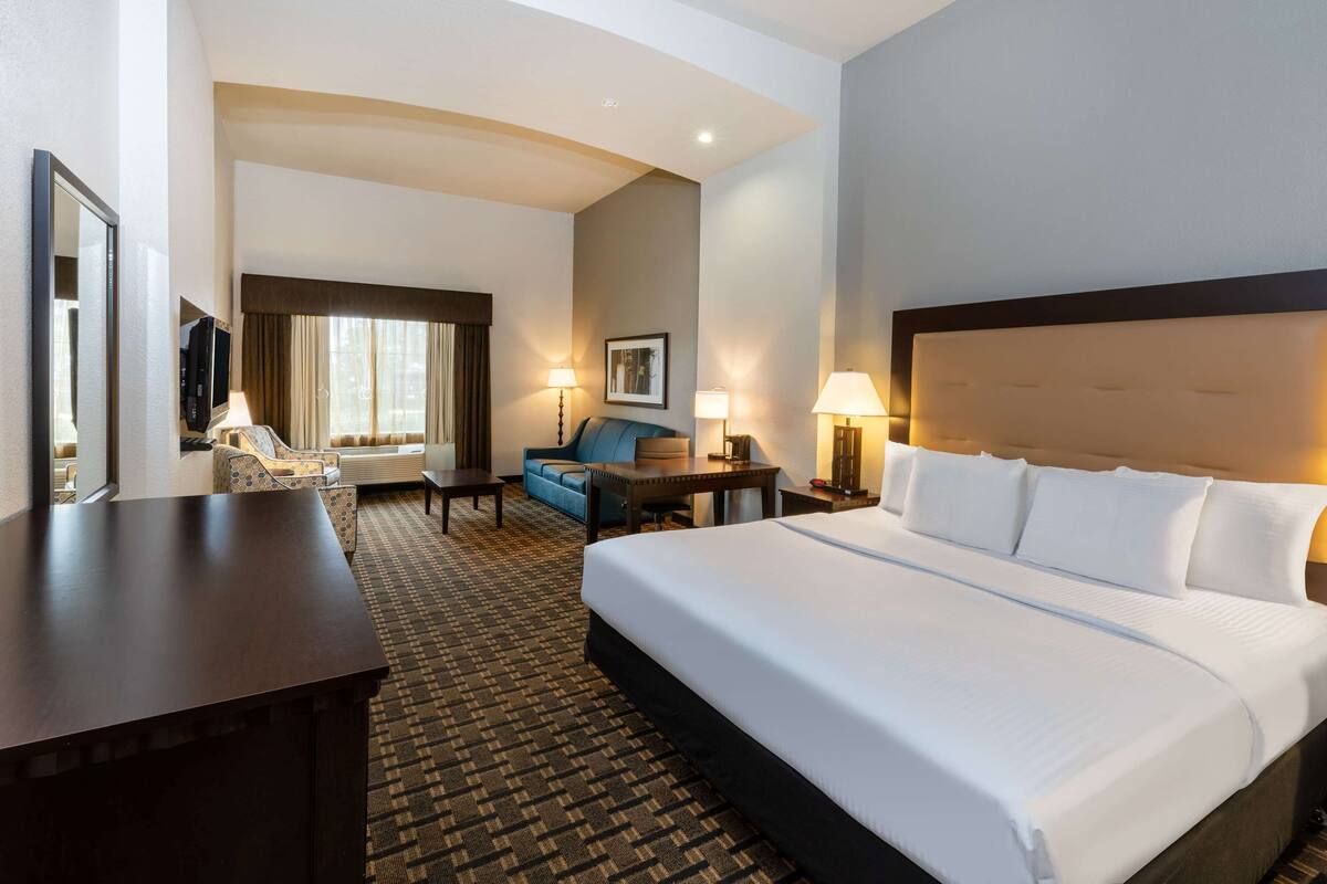 Ein Hotelzimmer mit einem großen Bett, einem Schreibtisch, einem Sessel, einer Couch und einem Fernseher.