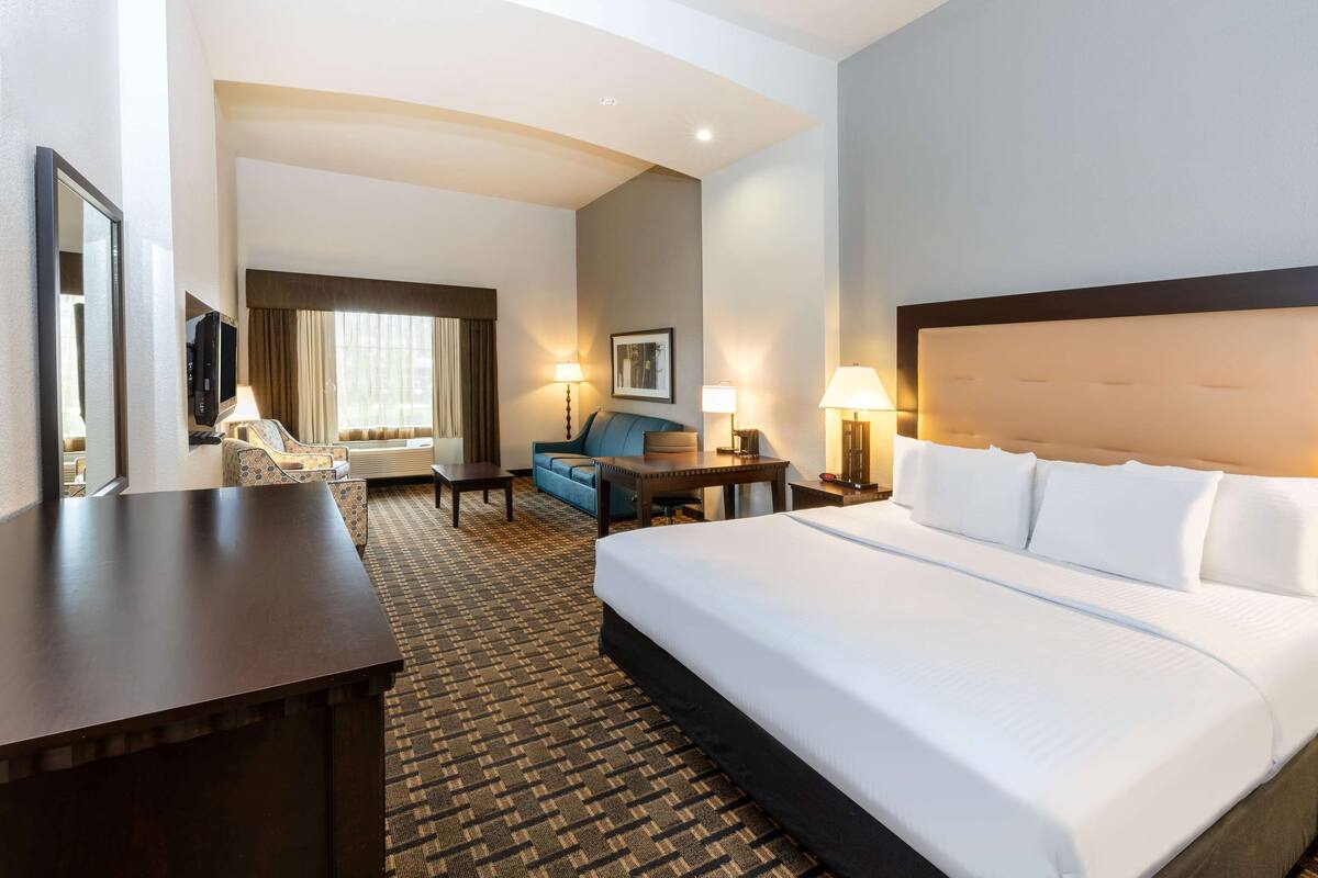 Ein Hotelzimmer mit einem großen Bett, einem Schreibtisch, einem Sessel, einer Couch und einem Fernseher.