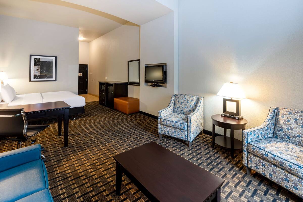 Ein Hotelzimmer mit einem Bett, zwei Sesseln, einer Couch, einem kleinen Tisch, einem Fernseher und einer Lampe.