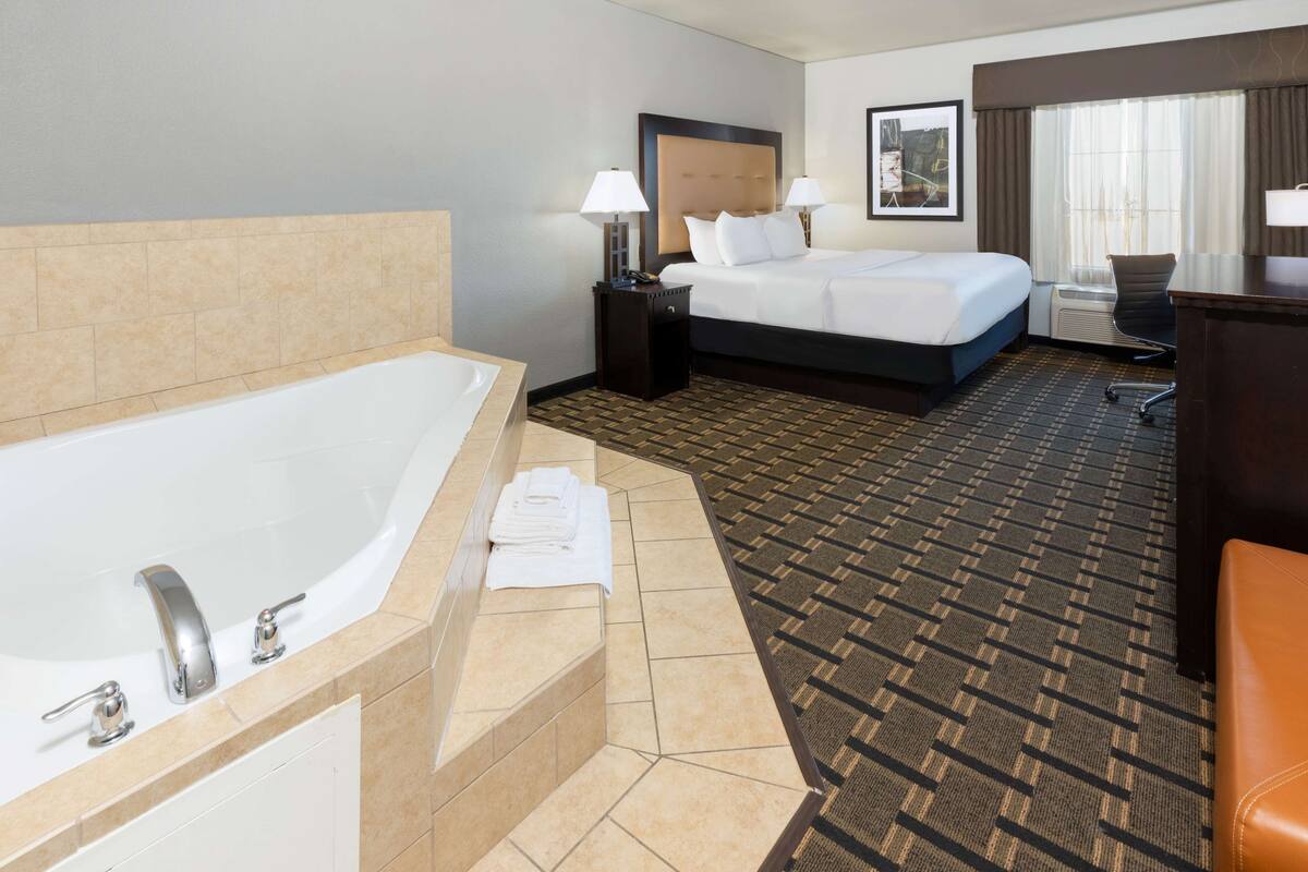 Ein Hotelzimmer mit einer großen Badewanne, einem Bett mit zwei Kissen, einem Schreibtisch und einem Stuhl.