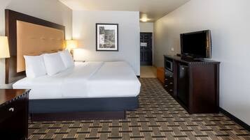 A hotel room with a large bed, a TV, a desk, and a framed picture on the wall.