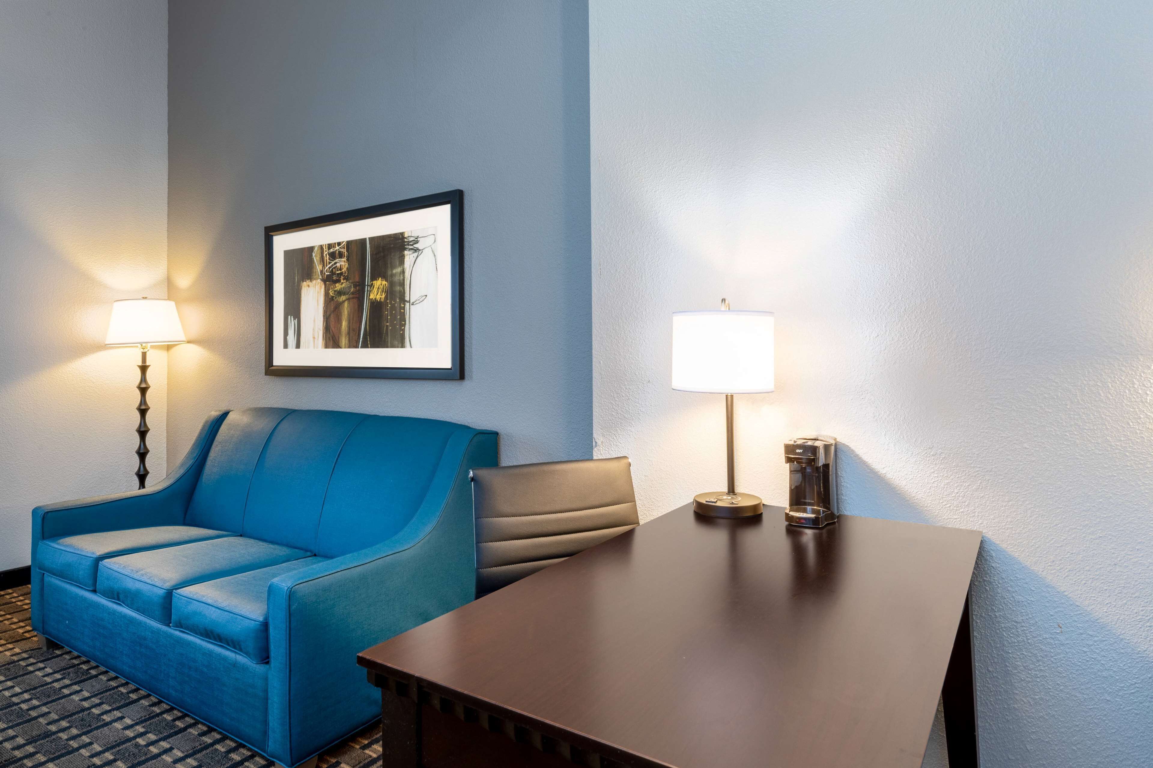 Habitación de hotel con un sofá azul, una mesita, una lámpara y un cuadro en la pared.