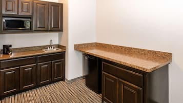 Una cocina compacta con armarios de madera oscura, encimera de granito, microondas integrado y lavavajillas.