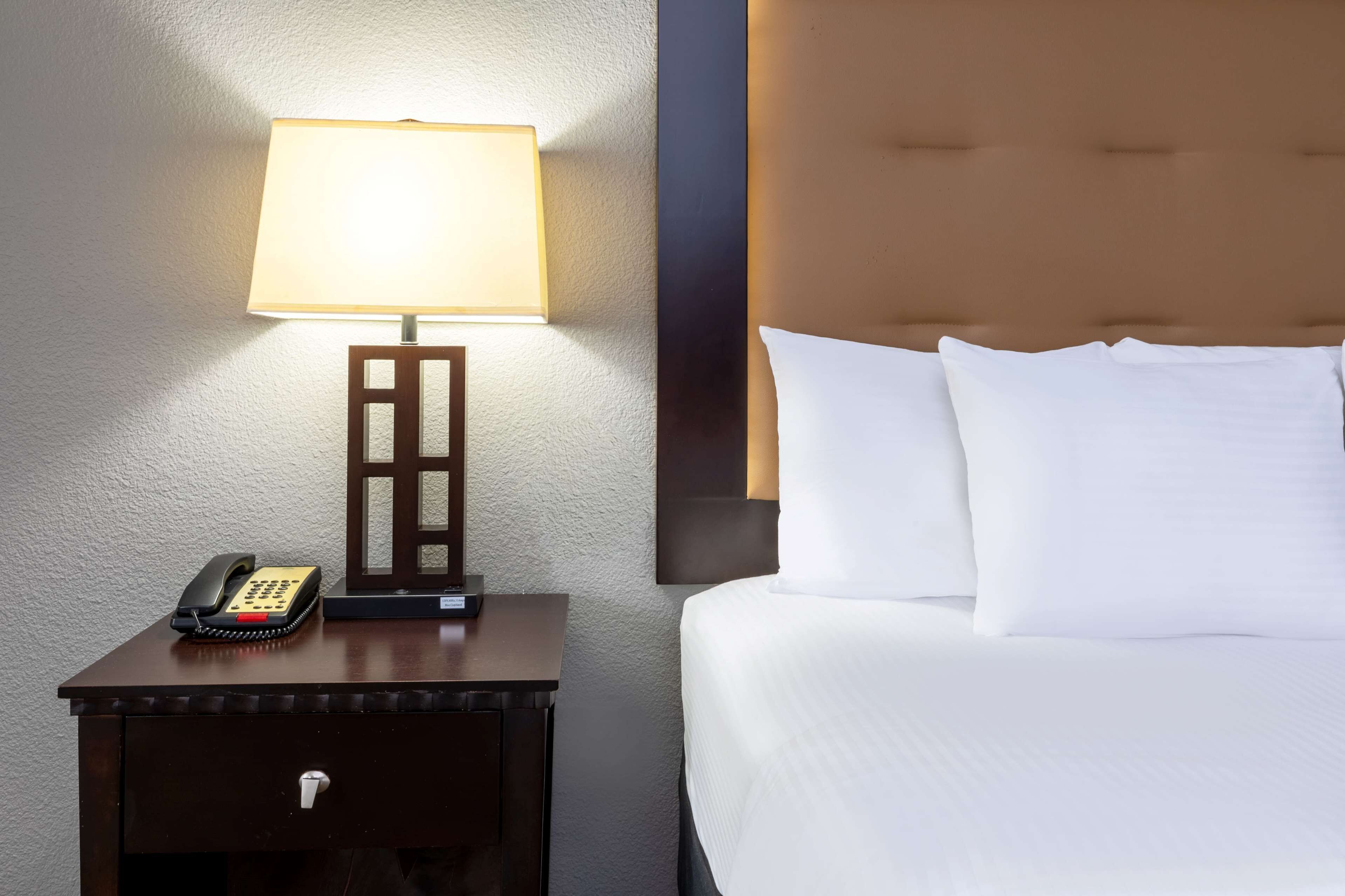 A hotel room with a bed, a nightstand with a lamp, and a telephone.