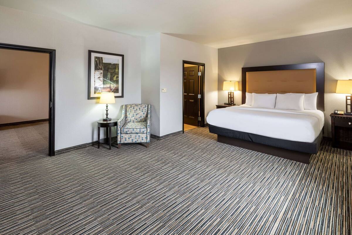 Ein Hotelzimmer mit einem großen Bett, einem Sessel, einem kleinen Tisch mit Lampe und einem gerahmten Bild an der Wand.