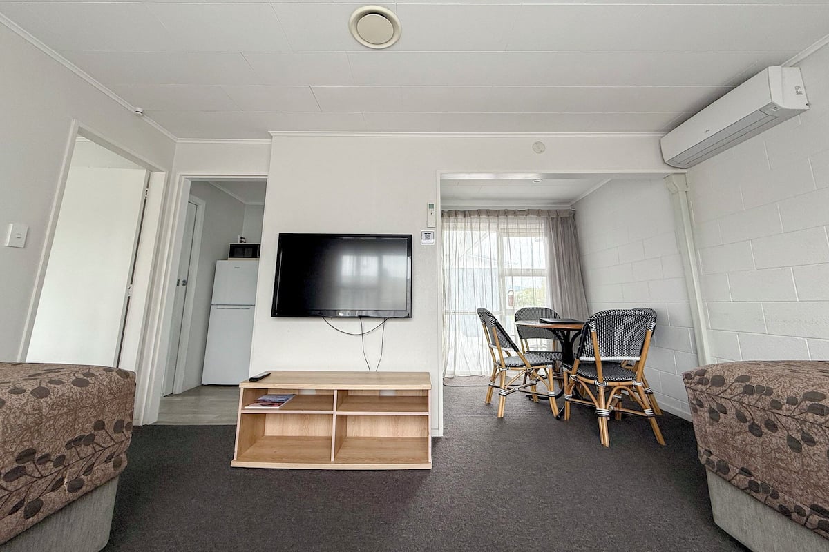 A living room with a flat-screen TV, a wooden TV stand, a dining table with chairs, and a sofa.