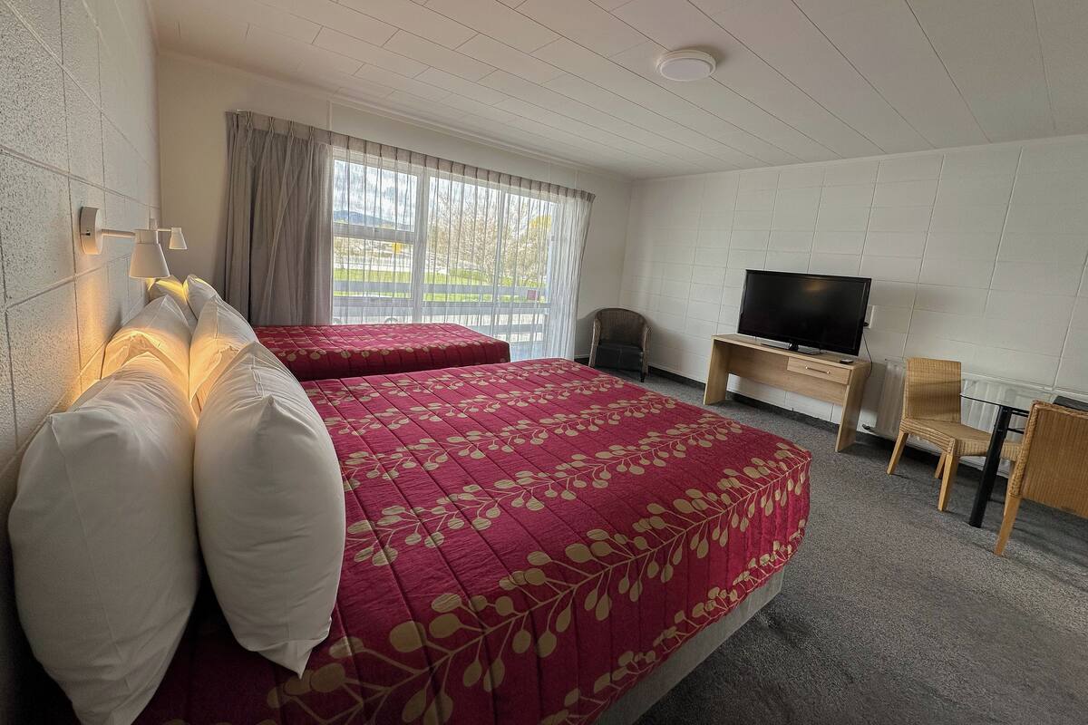 A hotel room with two beds, a TV, a desk, and a chair.