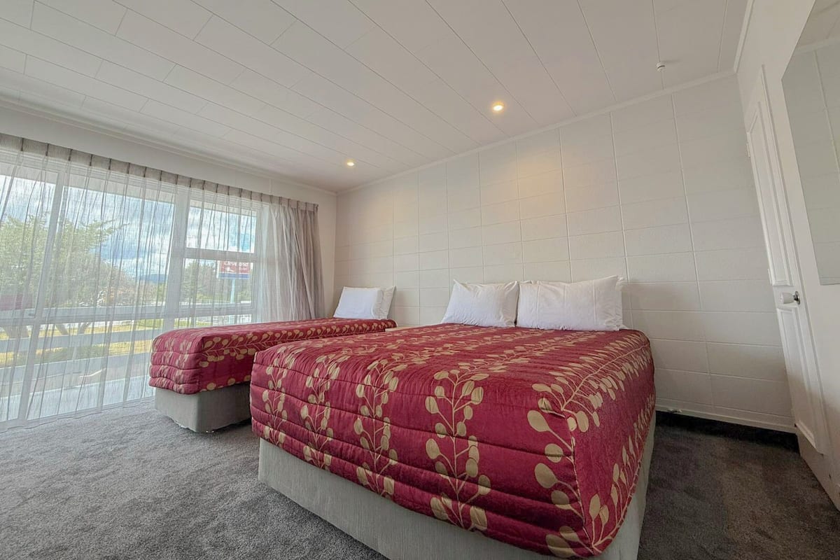A hotel room with a large bed, two bedside tables, a window with curtains, and a white tiled wall.