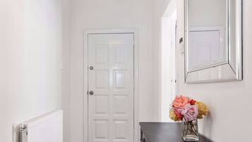 A hallway with a white door, a radiator, a dark wooden dresser, and a vase of flowers.