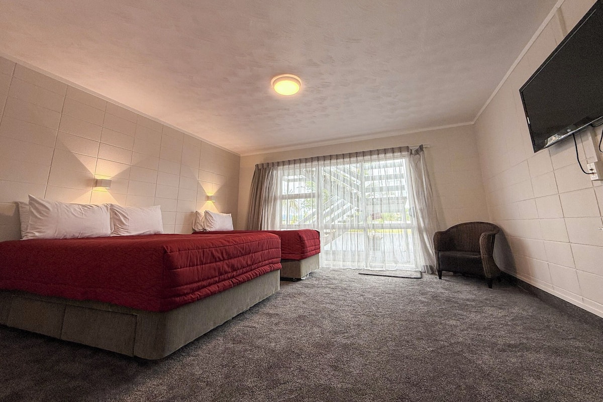 A hotel room with a bed, a chair, a TV, and a window with curtains.