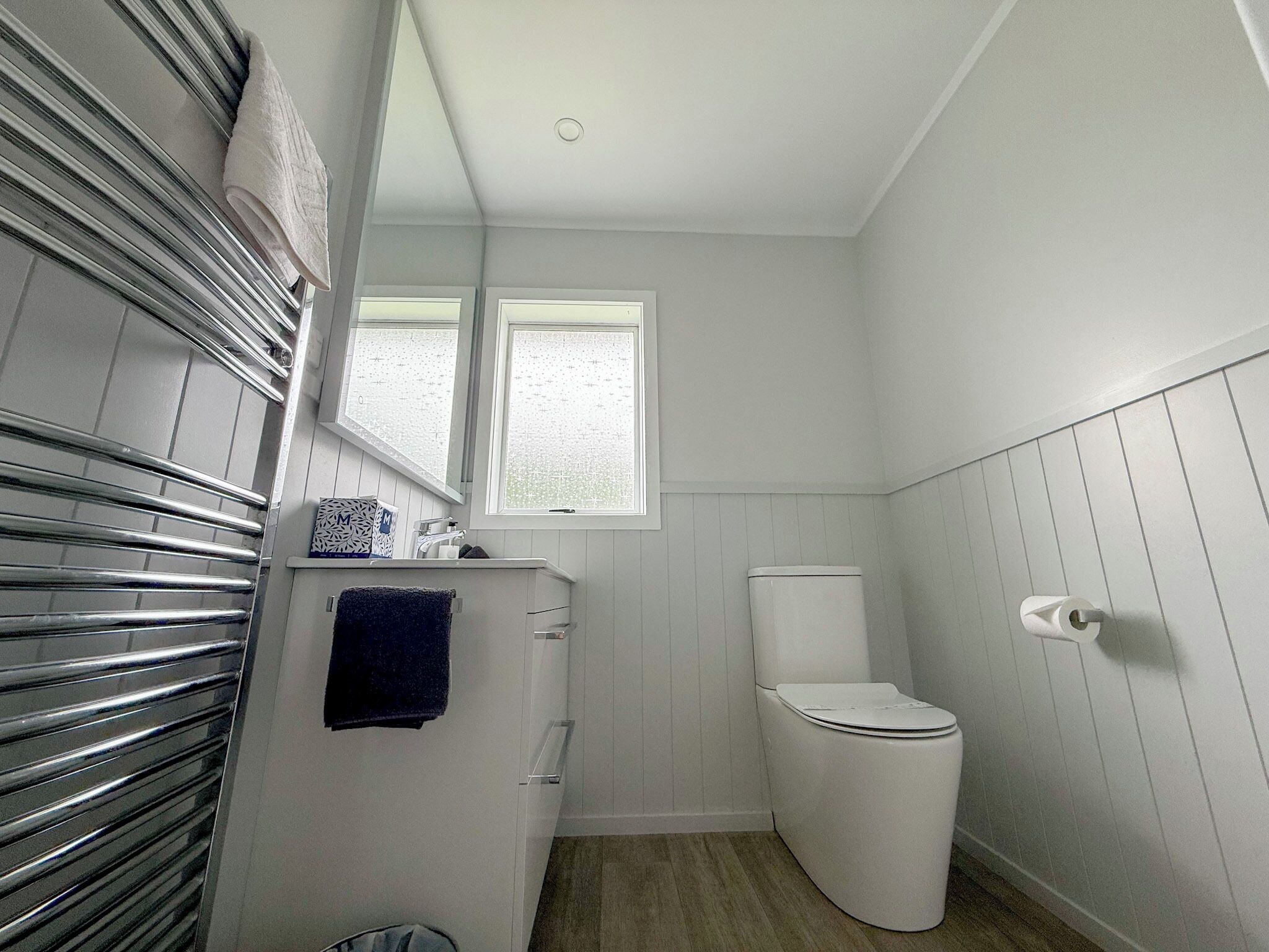 A compact bathroom with a toilet, a sink, a mirror, and a towel rack.