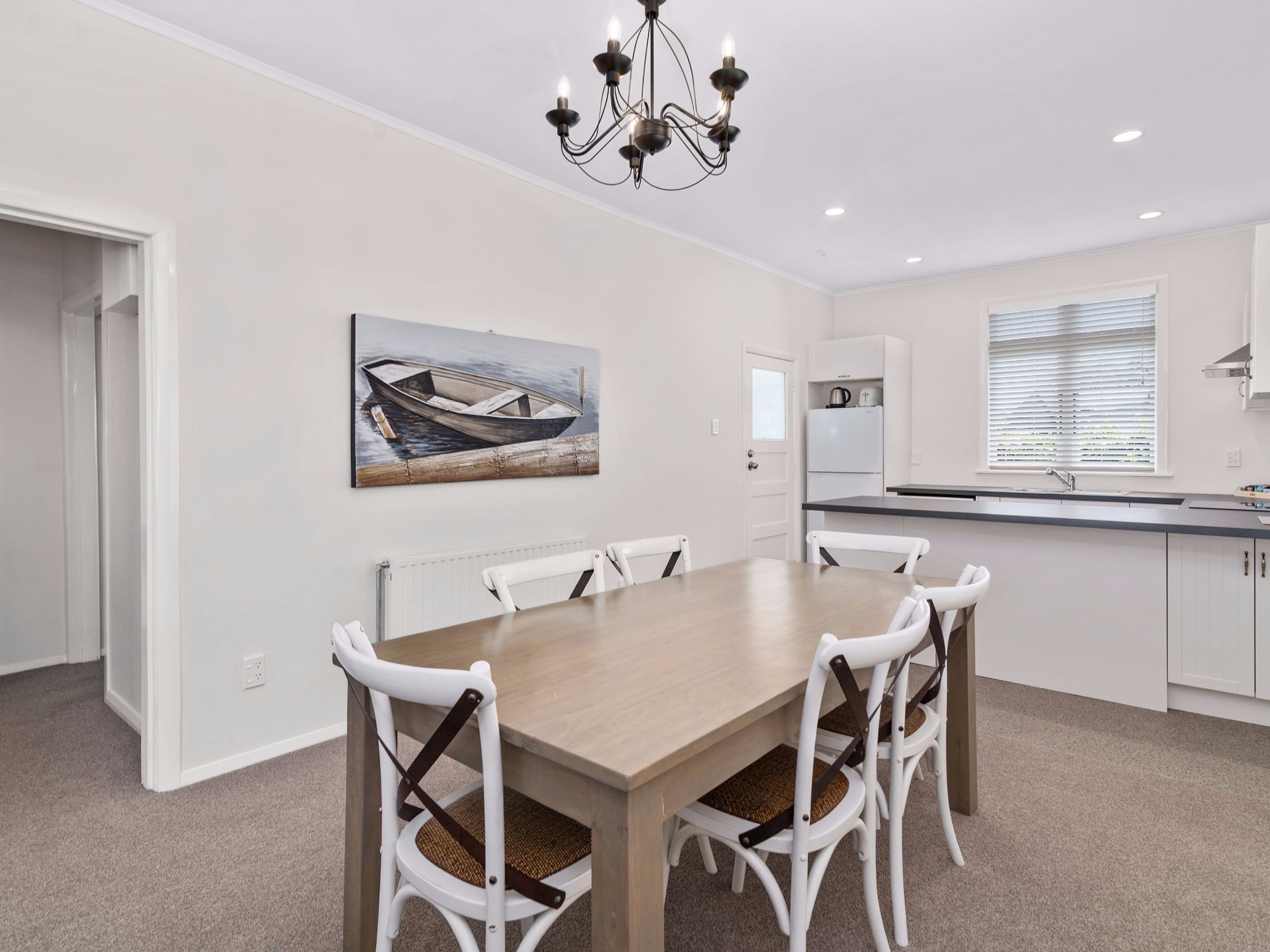 Een moderne keuken met witte kasten, een houten eettafel en een kroonluchter.