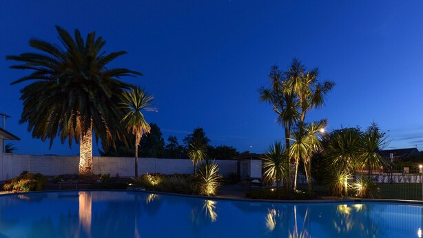 A swimming pool with palm trees and a stone wall in the background. - ASURE Cleveland Rotorua (Rotorua)