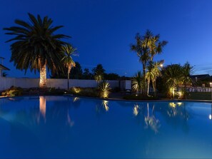 A swimming pool with palm trees and a stone wall in the background. - ASURE Cleveland Rotorua (Rotorua)