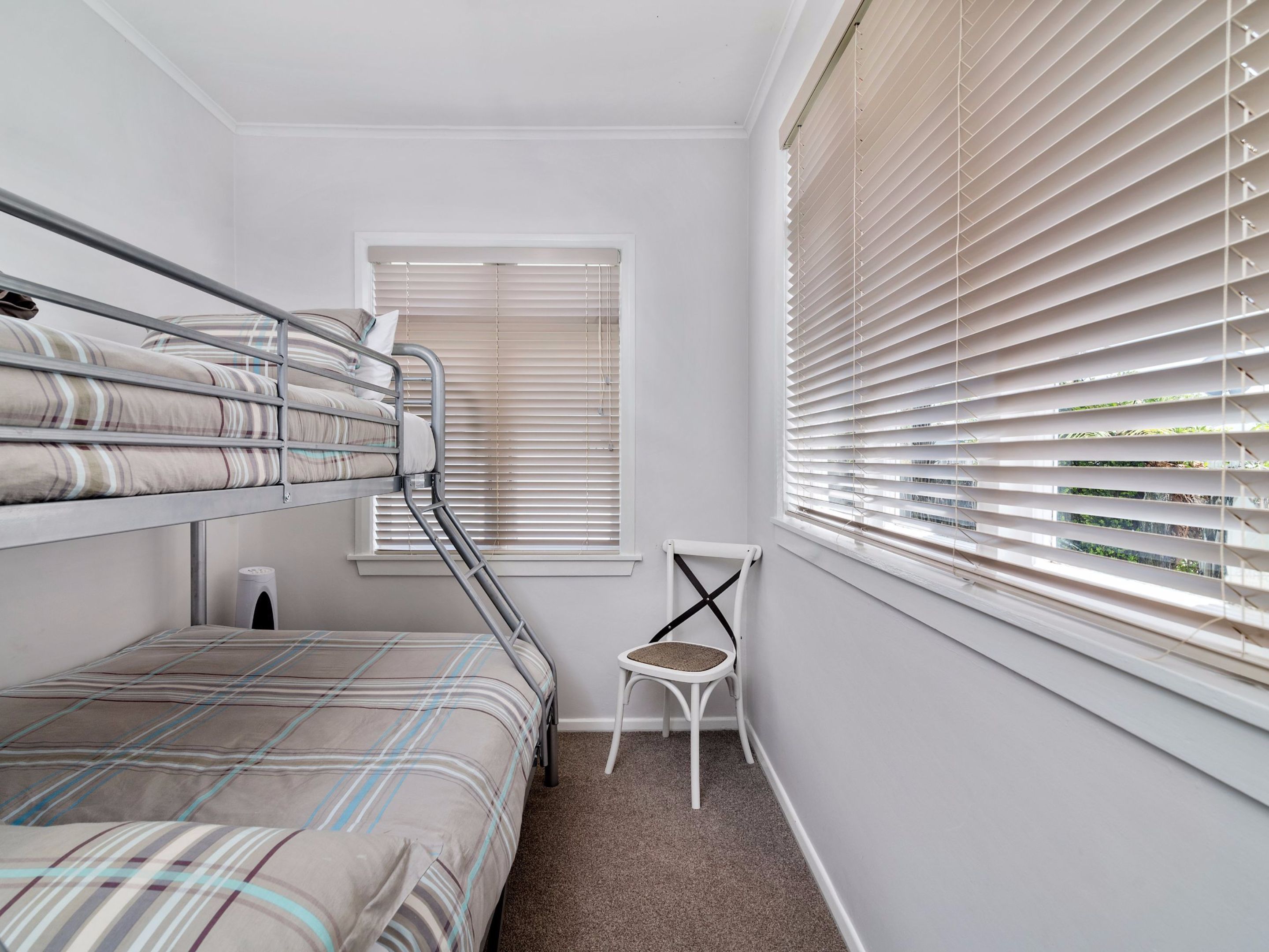 A small, well-lit room with bunk beds, a radiator, a window with blinds, and a chair.