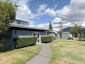A building with a paved walkway leading to a door, surrounded by a well-maintained lawn and a hedge. - ASURE Cleveland Rotorua (Rotorua)