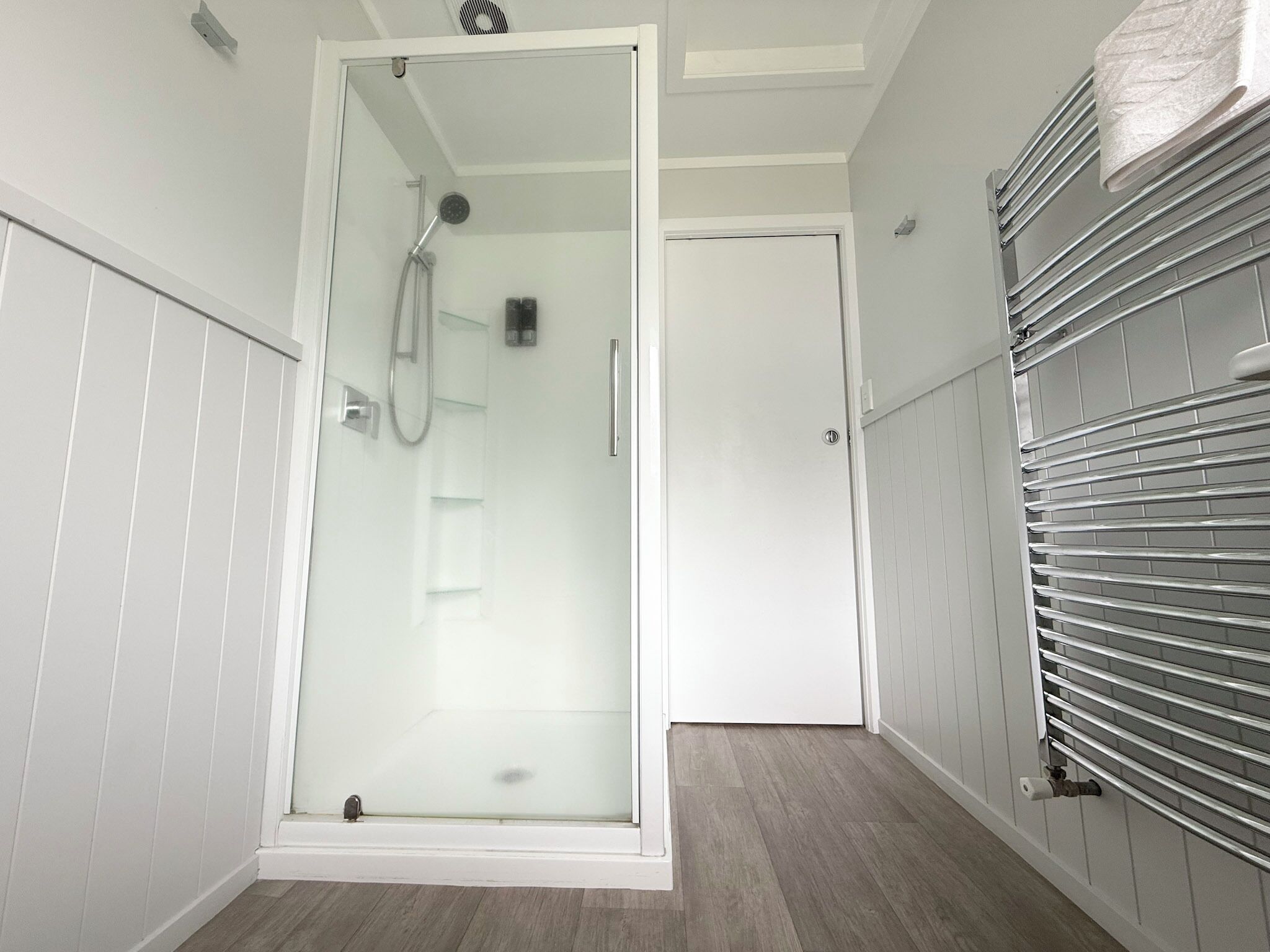Un baño moderno con ducha envuelta en vidrio, una puerta blanca y un perchero para toallas.
