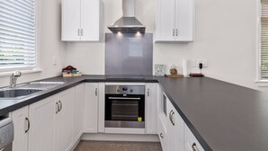 A modern kitchen with white cabinets, a stainless steel range hood, a built-in oven, and a black countertop. - ASURE Cleveland Rotorua (Rotorua)