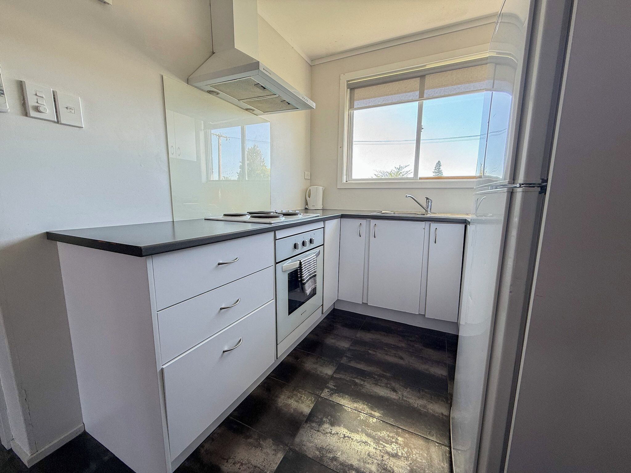 Una cocina compacta con gabinetes blancos, encimera negra, una ventana y una campana extractora de acero inoxidable.