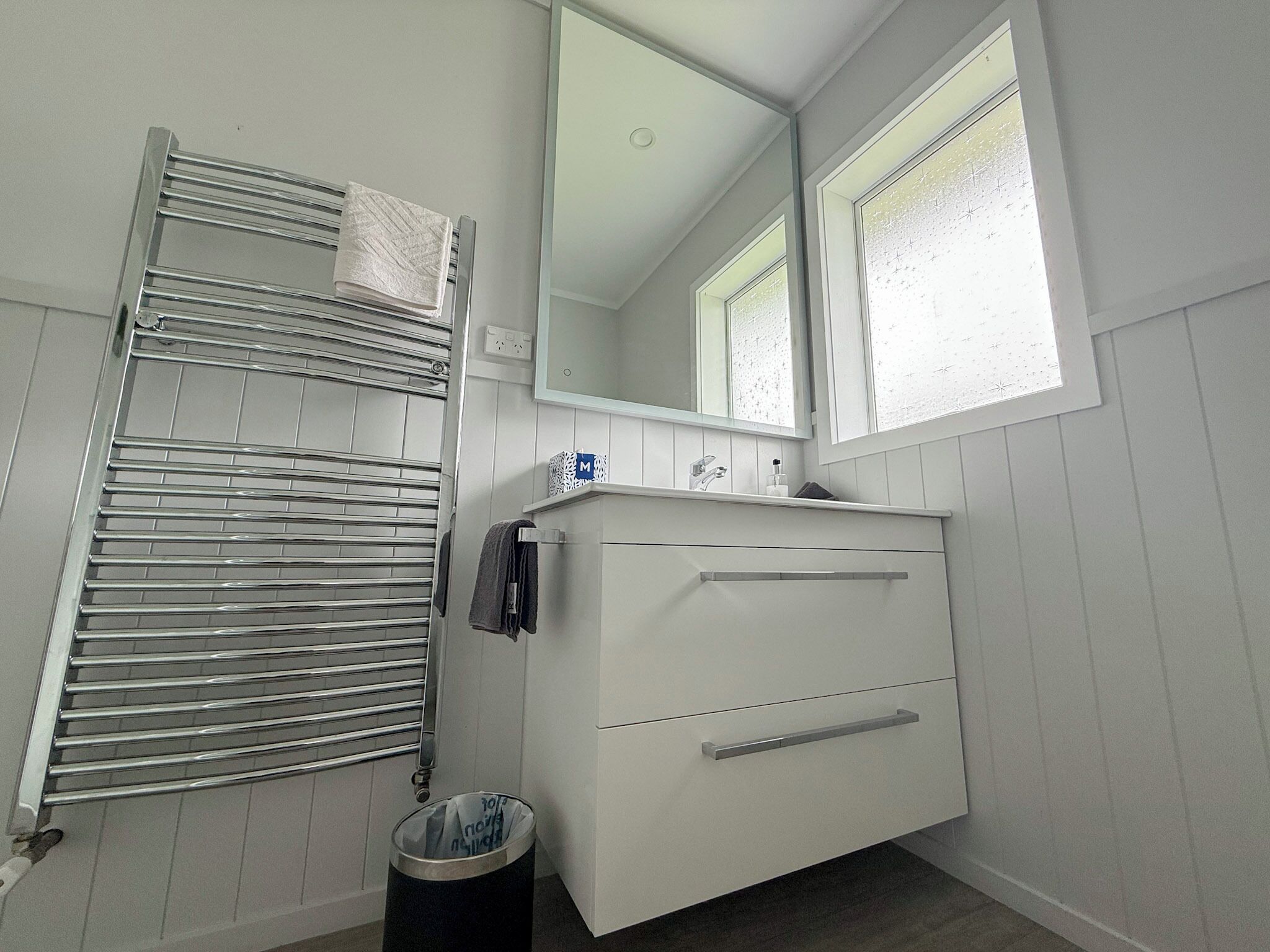 A bathroom with a white vanity, a towel rack, a mirror, and a window.