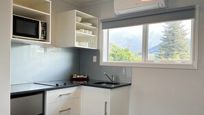 A modern kitchen with white cabinetry, a built-in microwave, a stainless steel refrigerator, and a window with a view of greenery and mountains. - ASURE Cleveland Rotorua (Rotorua)