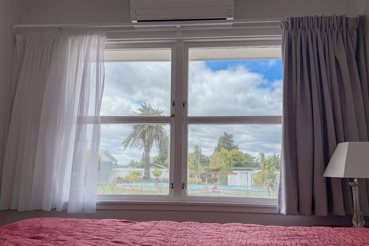 A room with a bed, a window with curtains, and an air conditioning unit.