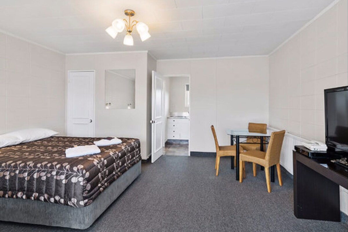 A hotel room with a bed, a desk, a chair, a television, and a mirror.