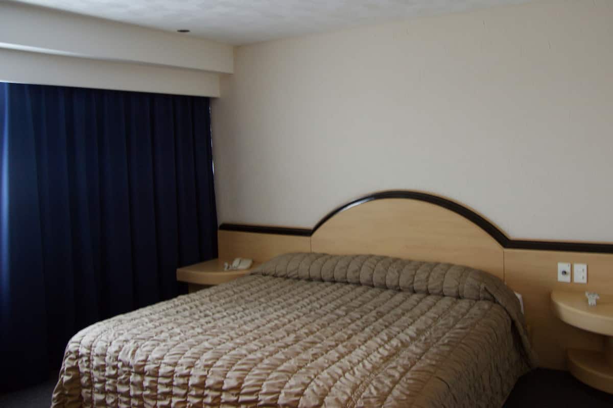 Habitación de hotel con cama, mesita de noche, teléfono y enchufe de pared.