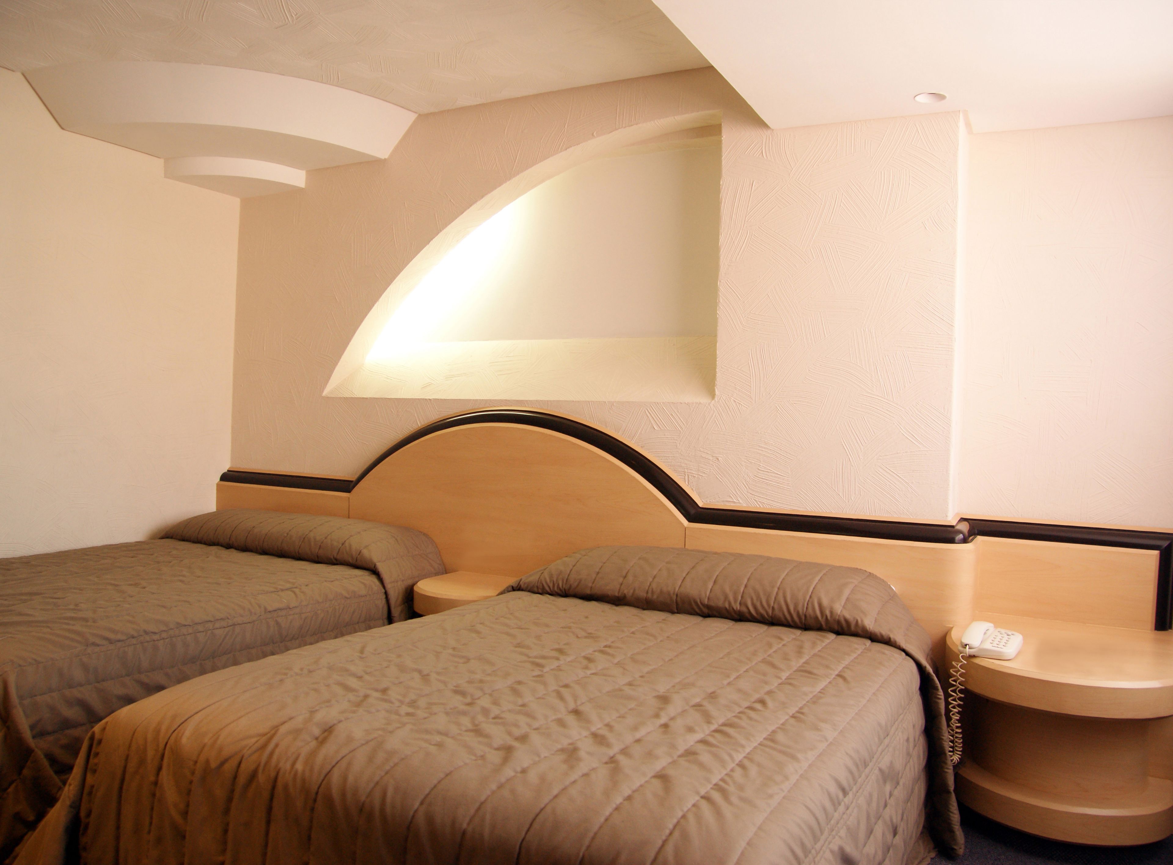 Een hotelkamer met twee bedden, een klein nachtkastje met een telefoon en een wandlamp.