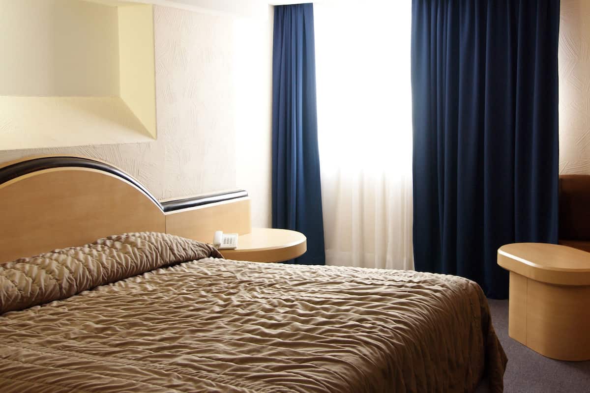 Una habitación de hotel con cama, mesitas de noche, teléfono y ventana con cortinas.