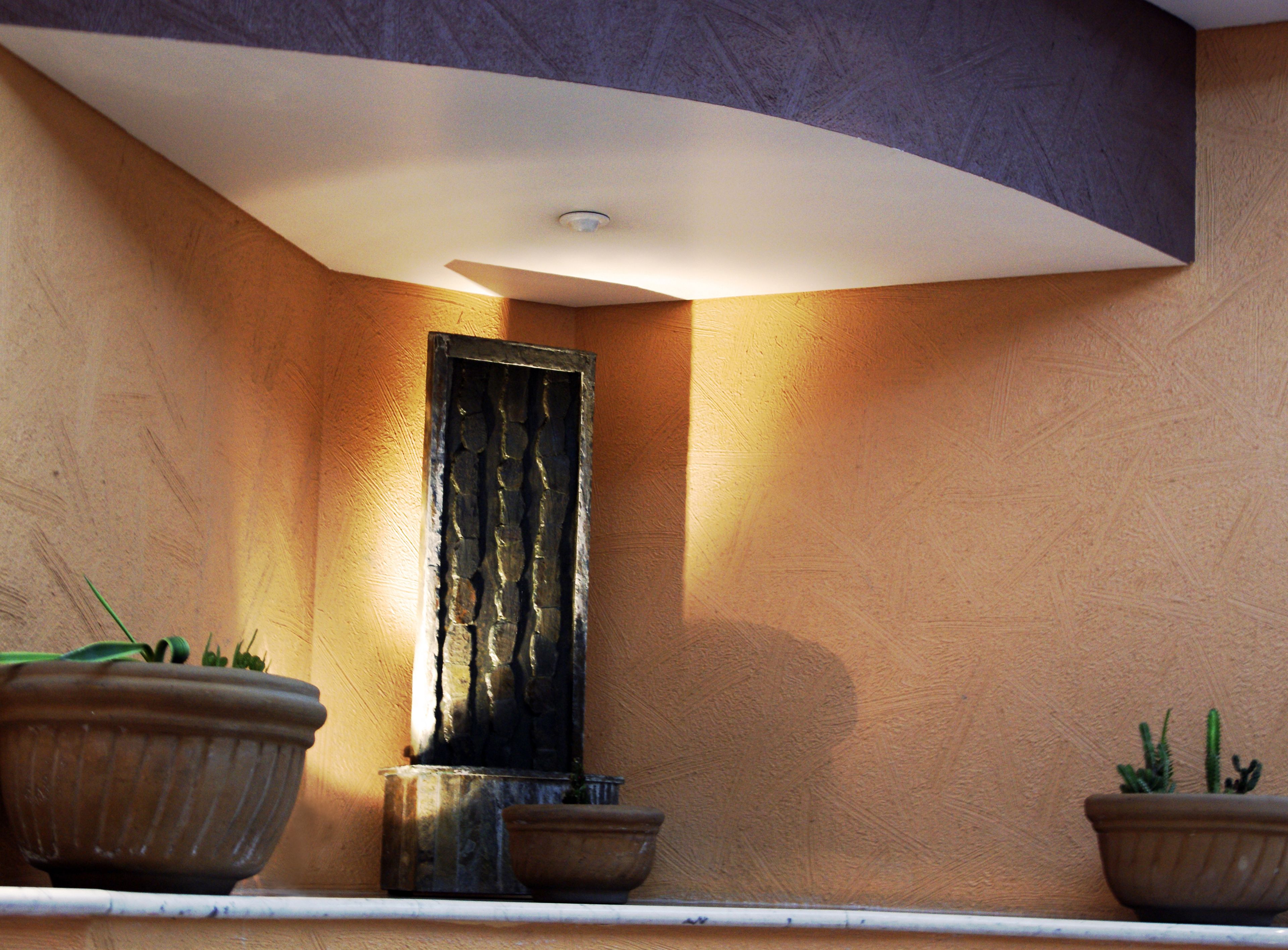 A wall-mounted rectangular mirror with a textured surface, flanked by two potted plants on either side.