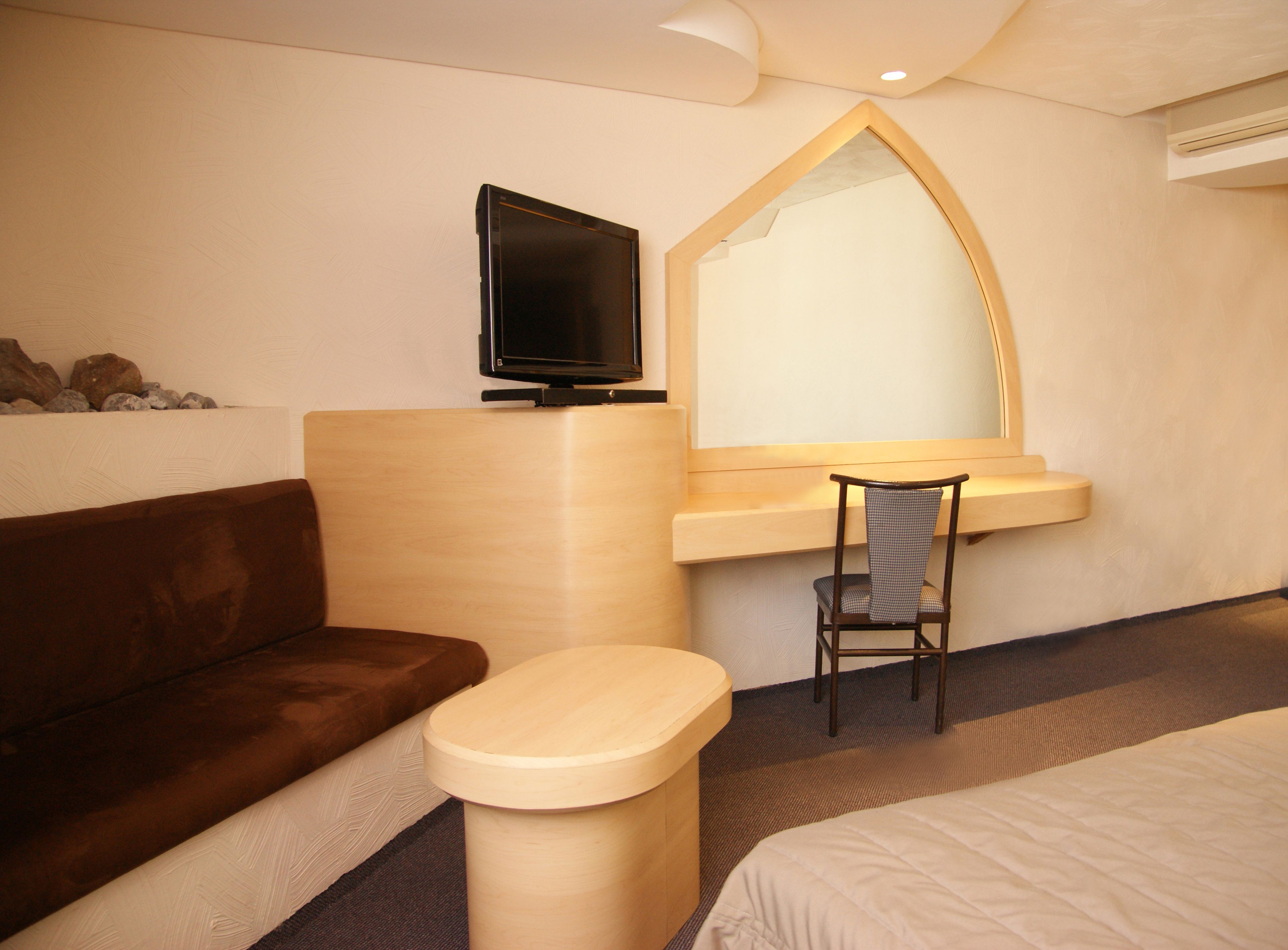 Una habitación de hotel con una cama, un escritorio de madera con una silla, un televisor y un espejo.
