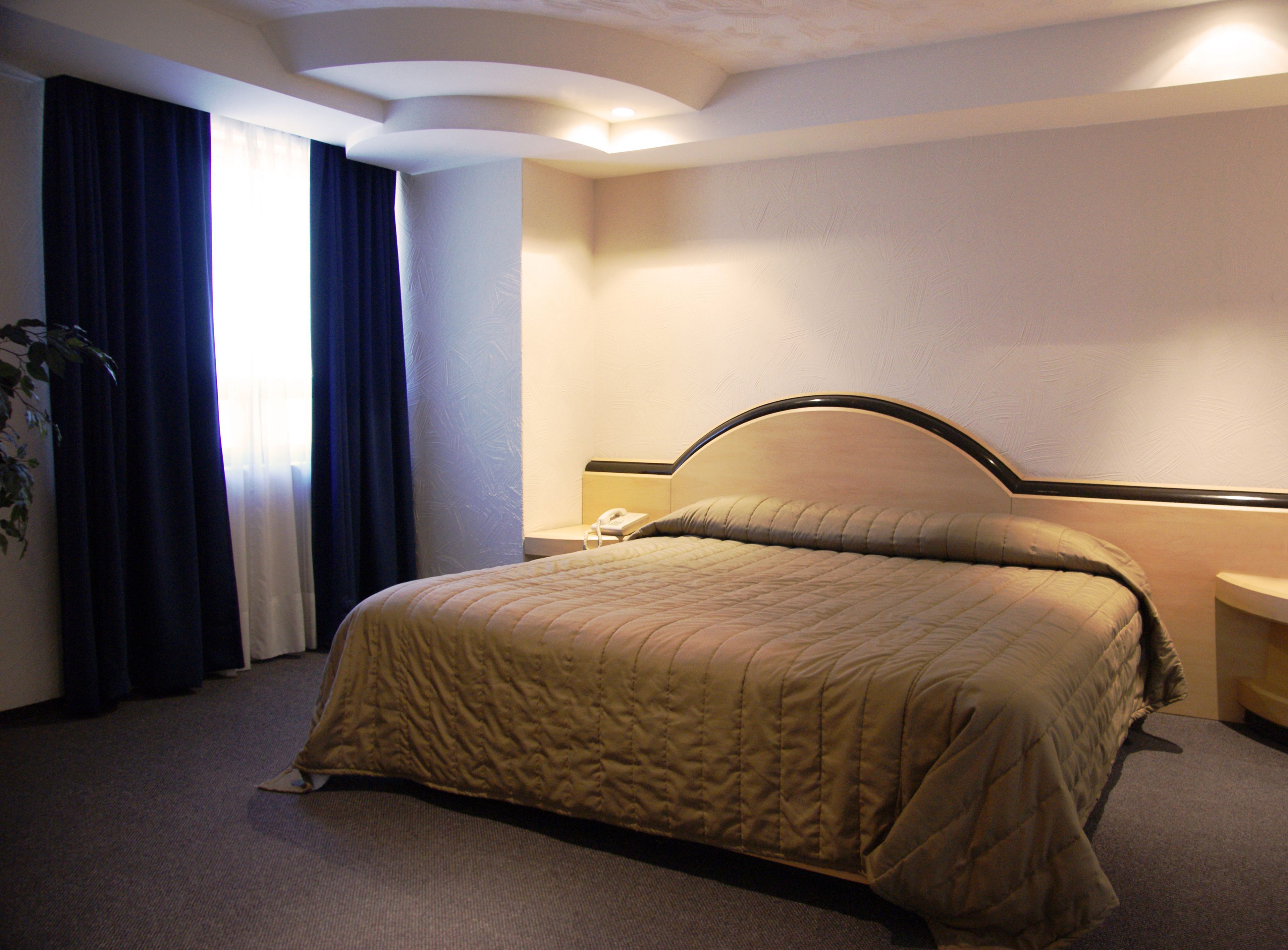 Une chambre d’hôtel avec un lit, une table de chevet, un téléphone et une fenêtre avec des rideaux.