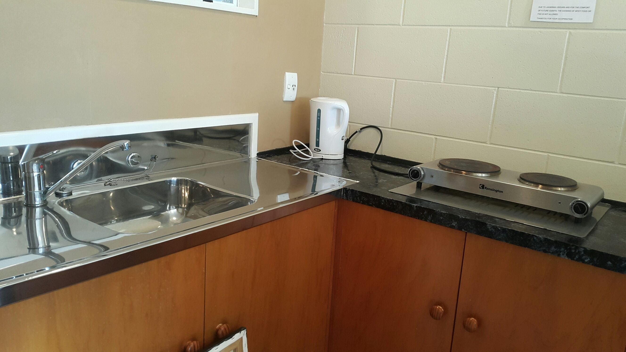 A kitchen with a stainless steel sink, a coffee maker, and a portable gas stove.