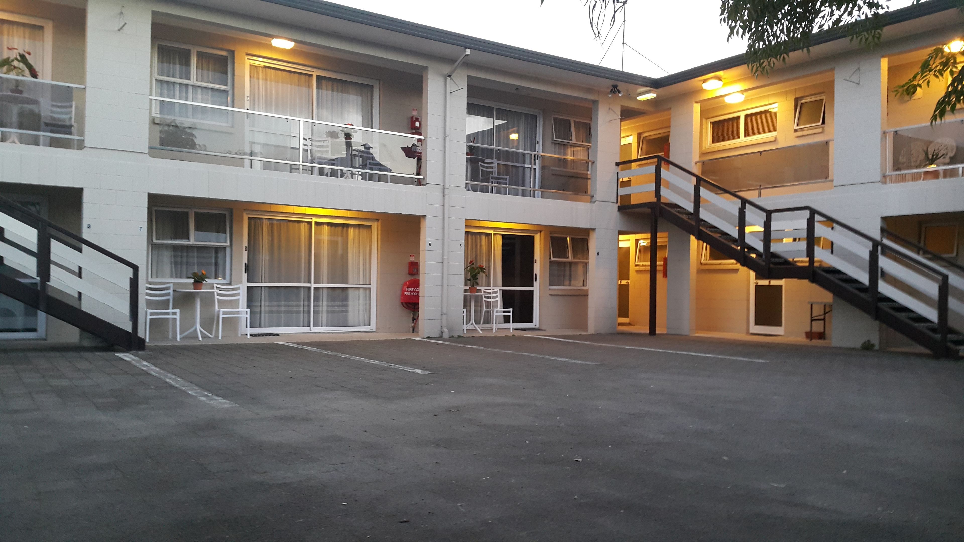 A multi-story motel with a covered outdoor seating area, a fire extinguisher, and a staircase.