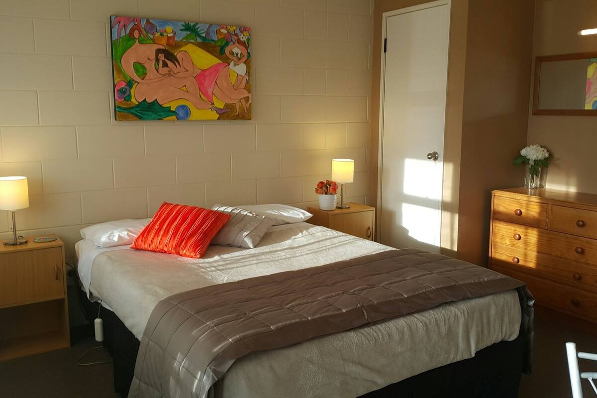 A bedroom with a bed, two bedside tables, a dresser, and a painting on the wall.