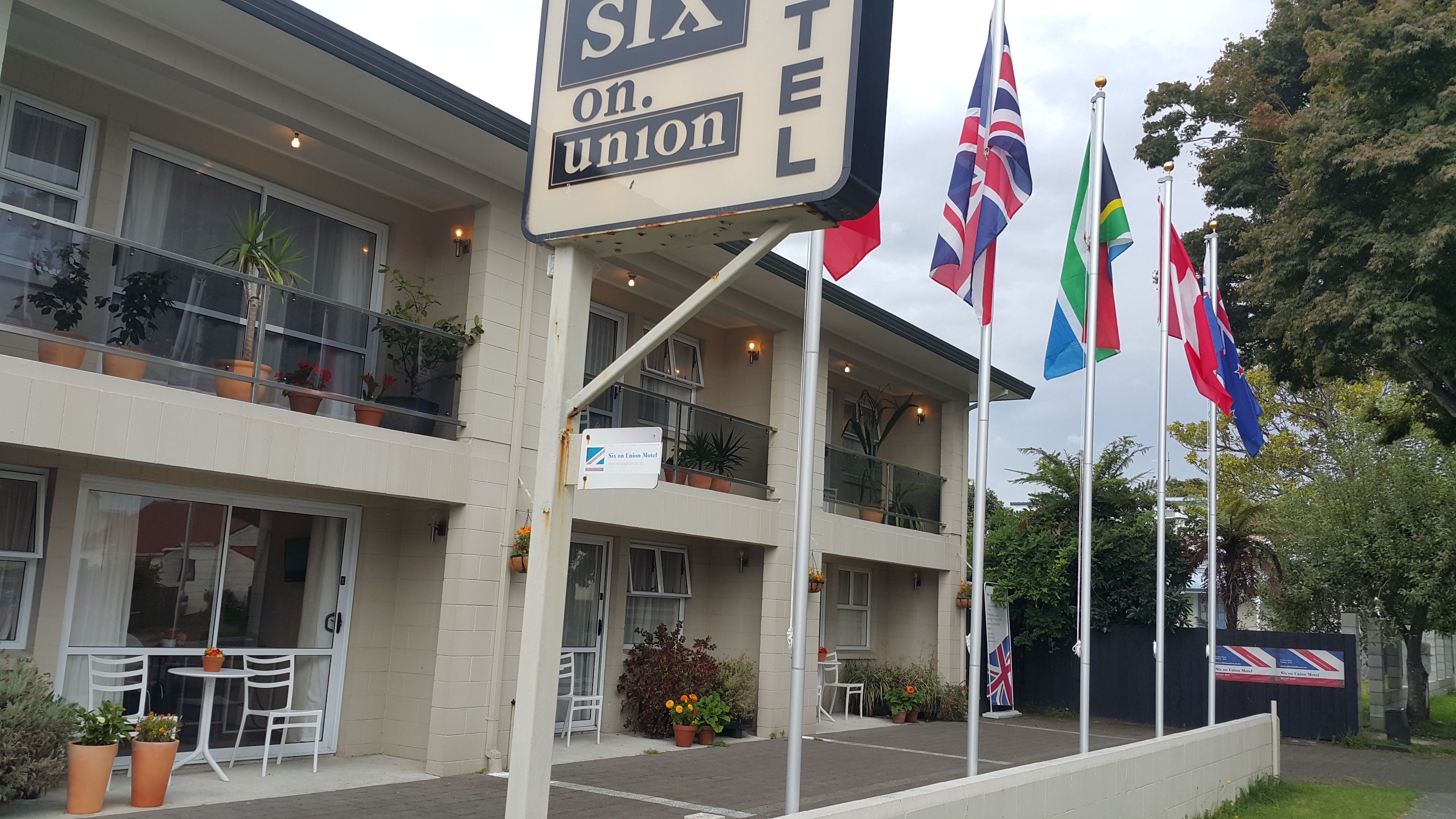 A hotel with a sign reading "Six on Union," featuring multiple flags, outdoor seating, and potted plants.