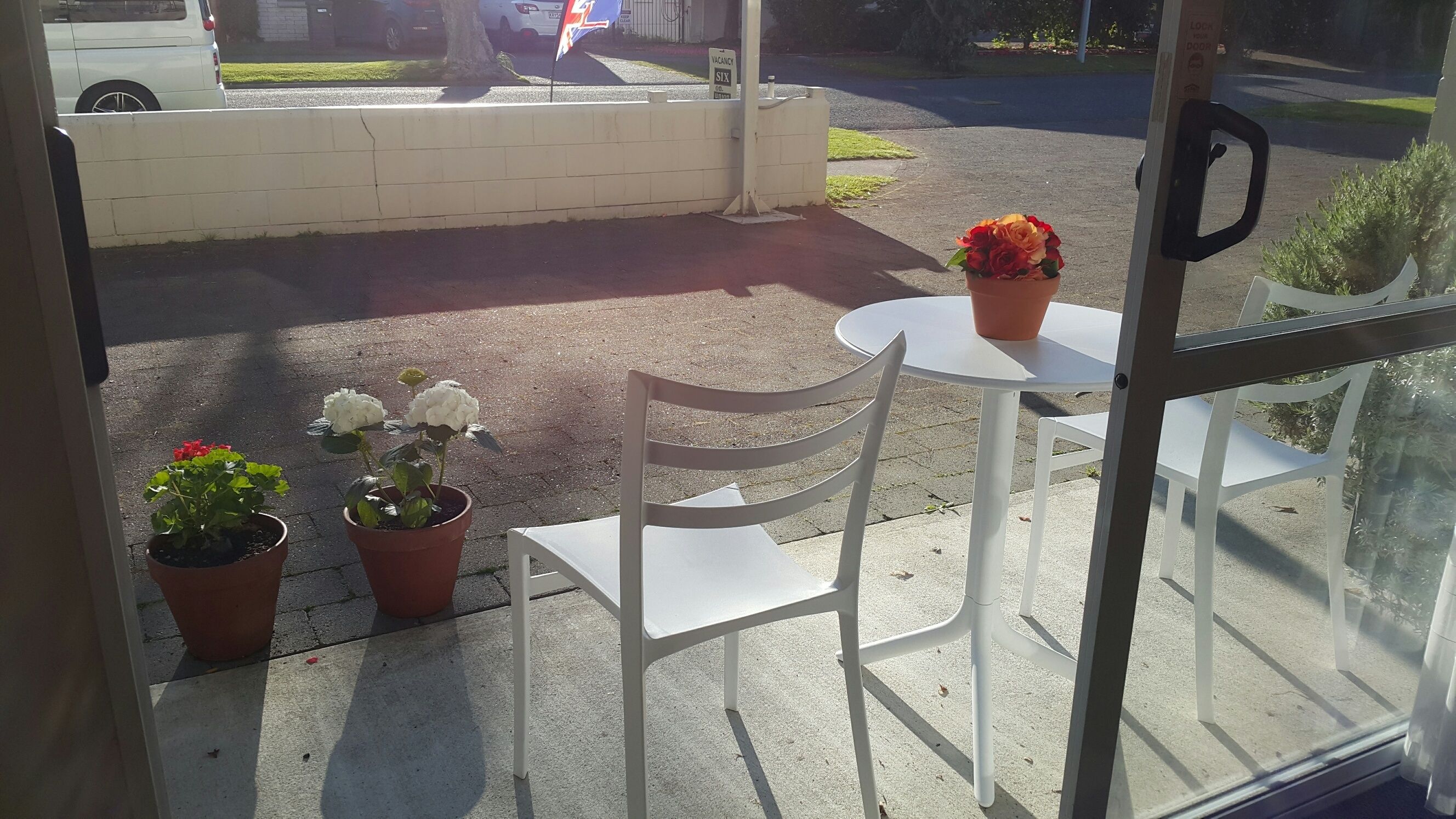 A view from inside a building looking out to a parking area with a white chair and table outside.